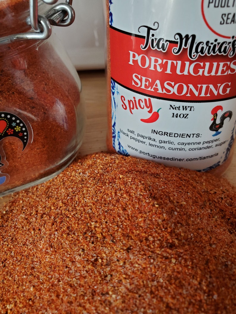 May include: A red and white jar filled with a red spice blend. The jar is labeled "Tia Maria's Portuguese Seasoning Spicy" and lists the ingredients: salt, paprika, garlic, cayenne pepper, black pepper, lemon, cumin, coriander, and sugar. The jar is 14 ounces.
