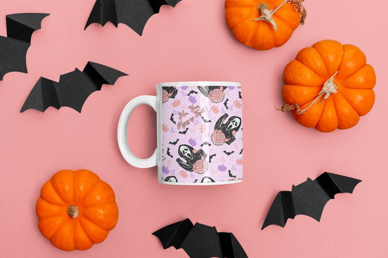 May include: White ceramic mug with a pink background and a repeating pattern of a ghost wearing a mask, bats, hearts, and pumpkins. The text "So, you wanna play?" is printed on the mug.