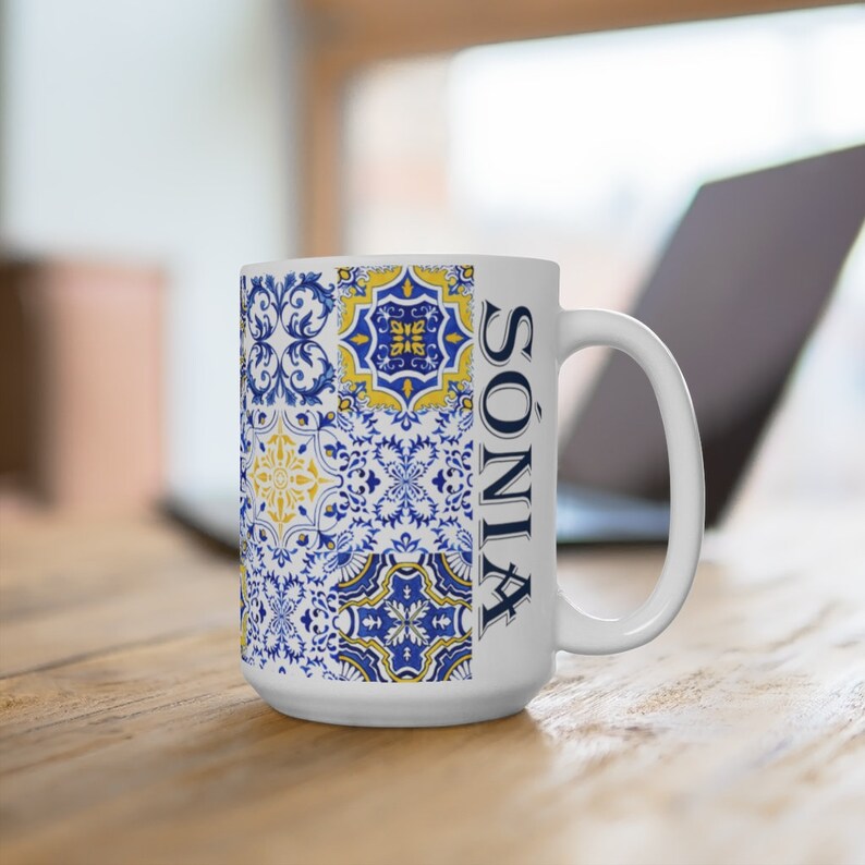 Puede incluir: Taza de cer&aacute;mica blanca con un dise&ntilde;o estampado en azul y amarillo. El patr&oacute;n recuerda a los azulejos portugueses tradicionales. La taza tiene el nombre "SONIA" escrito en el lateral.