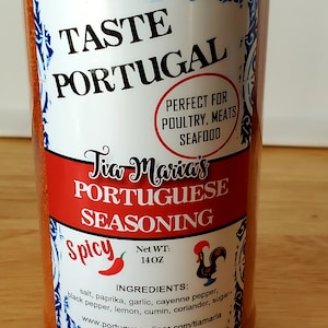 May include: A red plastic jar of Tia Maria's Portuguese Seasoning, labeled "Spicy" with a red chili pepper icon. The jar is 14 oz and contains ingredients like salt, paprika, garlic, cayenne pepper, black pepper, lemon, cumin, coriander, and sugar. The label also says "Taste Portugal" and "Perfect for Poultry, Meats, Seafood".