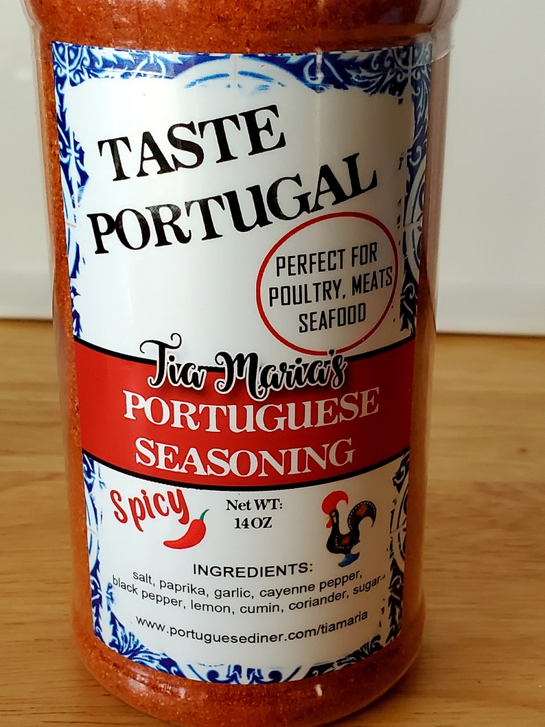 May include: A red plastic jar of Tia Maria's Portuguese Seasoning, labeled "Spicy" with a red chili pepper icon. The jar is 14 oz and contains ingredients like salt, paprika, garlic, cayenne pepper, black pepper, lemon, cumin, coriander, and sugar. The label also says "Taste Portugal" and "Perfect for Poultry, Meats, Seafood".
