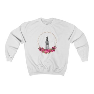 Pu&ograve; includere: Felpa bianca con una grafica di Nostra Signora di Fatima, una figura religiosa, circondata da rose rosa e una corona dorata.