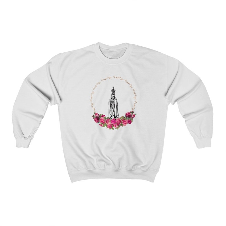 Pu&ograve; includere: Felpa bianca con una grafica di Nostra Signora di Fatima, una figura religiosa, circondata da rose rosa e una corona dorata.