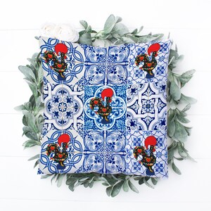 Pu&ograve; includere: Un cuscino blu e bianco con un motivo di piastrelle portoghesi con galli rossi. Il cuscino &egrave; decorato con un motivo ripetitivo di galli e forme geometriche.