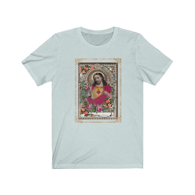May include: A light blue t-shirt with a vintage image of Jesus Christ in a gold frame with floral accents. The image is surrounded by pink roses and the word "Jesus" is printed below the image.