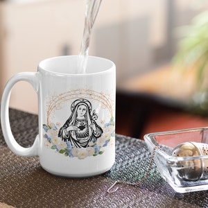 May include: White ceramic mug with a black and white image of the Virgin Mary with a heart and flowers. The mug is filled with water.