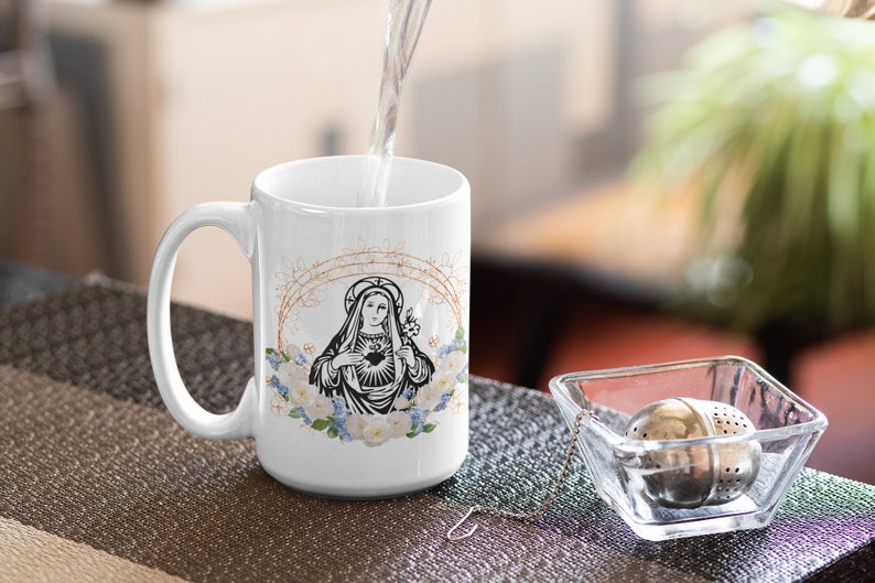 May include: White ceramic mug with a black and white image of the Virgin Mary with a heart and flowers. The mug is filled with water.