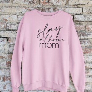 May include: Pink sweatshirt with the text "slay at home mom" in black lettering.