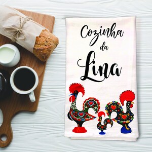 May include: White kitchen towel with the text "Cozinha da Lina" in black cursive lettering. Two colorful Portuguese roosters are depicted at the bottom of the towel.