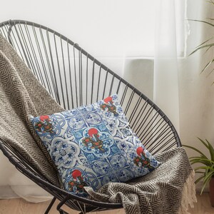 Pu&ograve; includere: Una sedia in metallo nero con un cuscino decorativo a motivi bianchi e blu. La sedia &egrave; coperta da una coperta marrone e bianca. Una pianta verde &egrave; in un vaso marrone sullo sfondo.