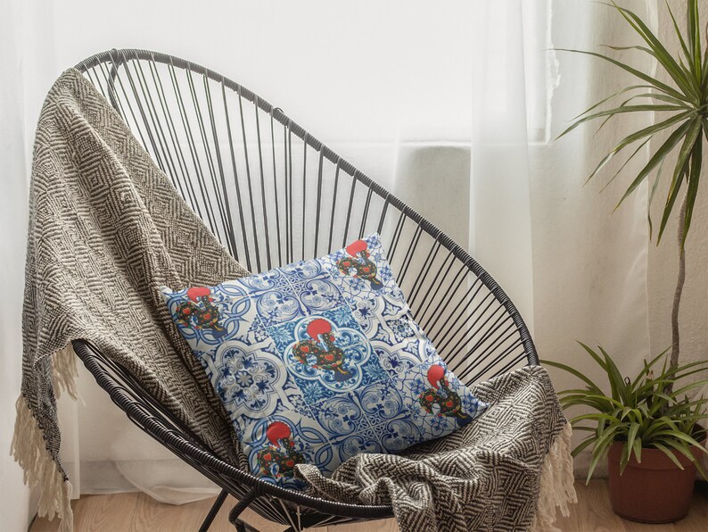 Pu&ograve; includere: Una sedia in metallo nero con un cuscino decorativo a motivi bianchi e blu. La sedia &egrave; coperta da una coperta marrone e bianca. Una pianta verde &egrave; in un vaso marrone sullo sfondo.