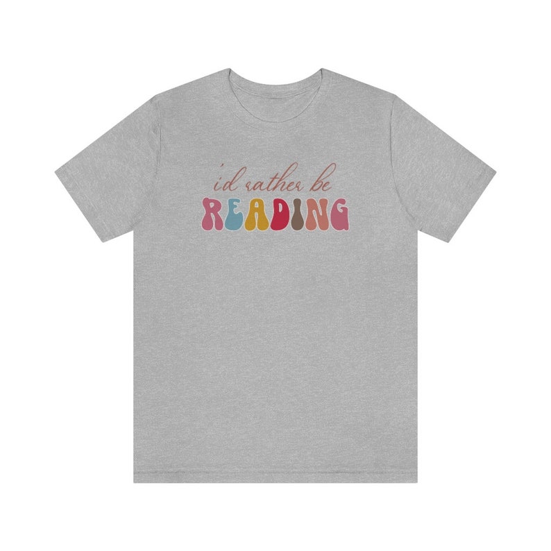Puede incluir: Una camiseta gris jaspeada con el texto "i'd rather be READING" en letras de colores de estilo retro.