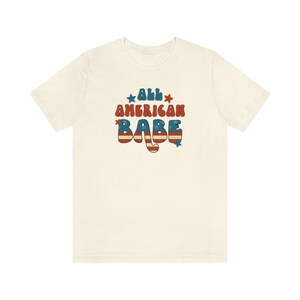 May include: A white t-shirt with a red, white and blue graphic that says "All American Babe" in a retro font.