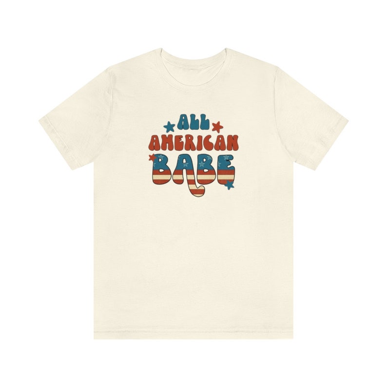 May include: A white t-shirt with a red, white and blue graphic that says "All American Babe" in a retro font.