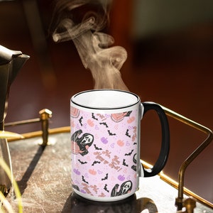 May include: White ceramic mug with a black handle. The mug has a pink background with a repeating pattern of a ghost holding a pumpkin, bats, and hearts. The text on the mug reads "You got this!  No,  Huny yo Sret!"