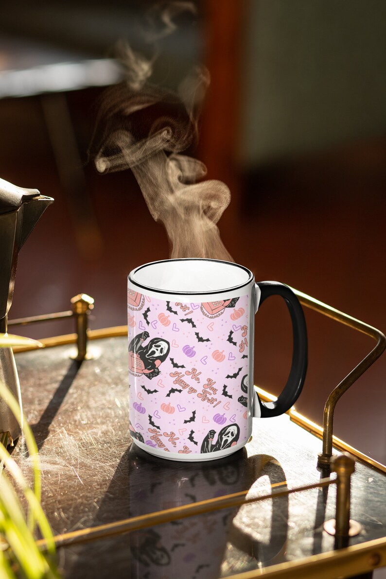 May include: White ceramic mug with a black handle. The mug has a pink background with a repeating pattern of a ghost holding a pumpkin, bats, and hearts. The text on the mug reads "You got this!  No,  Huny yo Sret!"