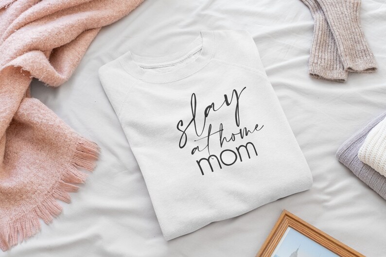May include: White t-shirt with black text that reads "slay at home mom".