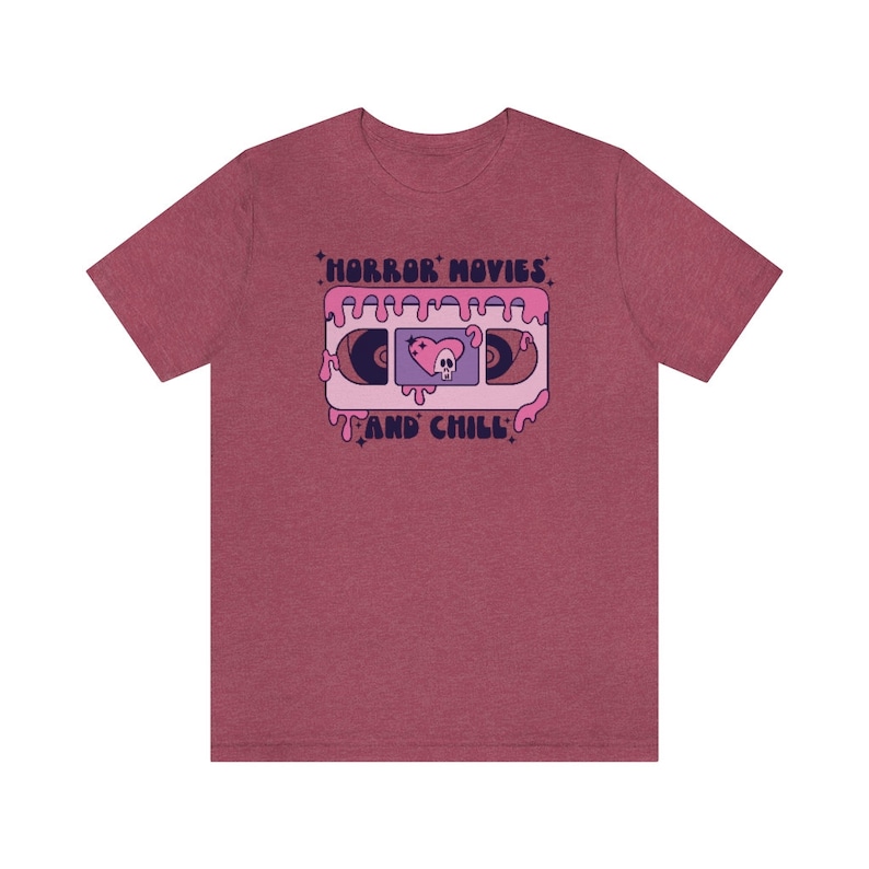 May include: A heather red t-shirt with a graphic of a pink VHS tape with the text "HORROR MOVIES AND CHILL" in a retro font.
