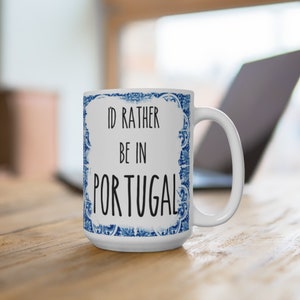 May include: White ceramic mug with a blue and white patterned design. The mug has the text "I'd rather be in Portugal" printed on it.