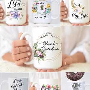 May include: A collection of white ceramic mugs with various designs and text. The mugs feature floral designs, a bee, a moon, and text such as "Aunt Lisa", "Queen Bee", "Mrs. Costa", "Blessed Grandma", "More espresso. Less depresso", "Portuguesa", and "Shopping is cheaper than therapy".