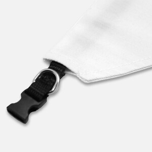May include: Close-up of a white fabric triangle with a black nylon strap, a silver metal D-ring, and a black plastic buckle. The fabric is stitched along the edges.