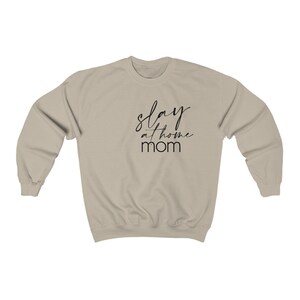 May include: A light beige sweatshirt with the text "slay at home mom" printed in black.