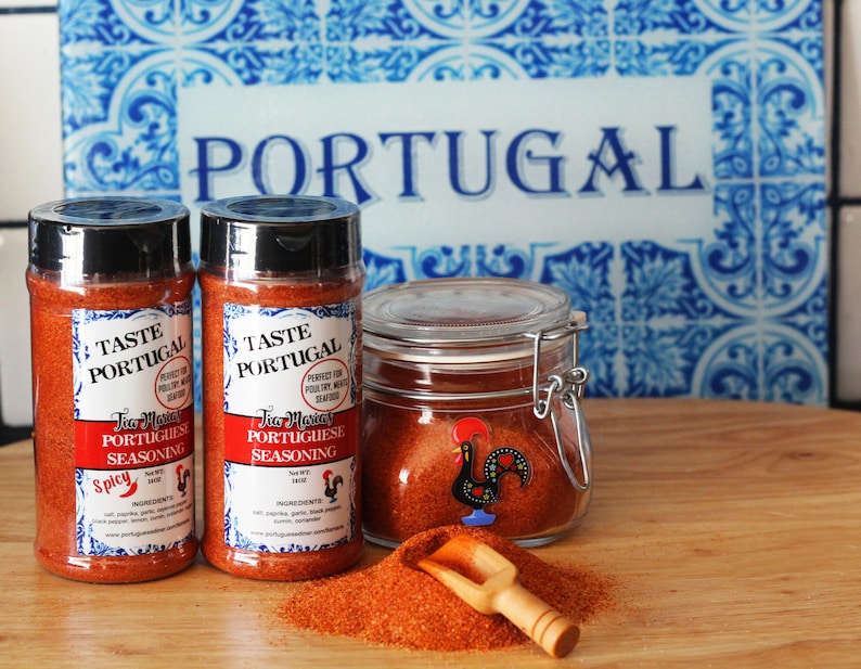 May include: Two glass jars of red Portuguese seasoning with a rooster logo and the text "Taste Portugal Tia Maria Portuguese Seasoning Spicy" on the label. A small wooden scoop is next to a pile of the red seasoning.