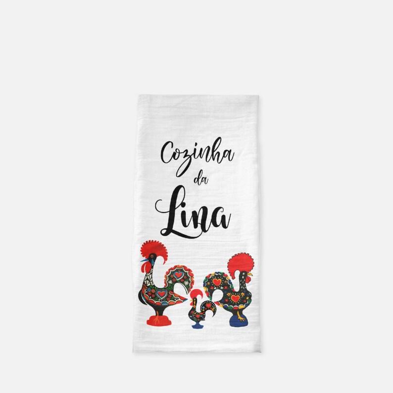 May include: White kitchen towel with the text "Cozinha da Lina" in black cursive lettering. Two black, red, and blue rooster figurines are at the bottom of the towel.