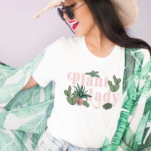 May include: White t-shirt with the text "Plant Lady" in pink lettering and a graphic of cacti and succulents.