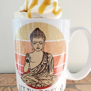 K&ouml;nnte beinhalten: Eine wei&szlig;e Keramiktasse mit einer Grafik eines meditierenden Buddha in einem kreisf&ouml;rmigen Sonnenuntergangsmuster. Der Text "Let That Shit Go" ist unter dem Buddha aufgedruckt. Die Tasse hat einen wei&szlig;en Henkel und ist mit Schlagsahne und Karamellso&szlig;e verziert.