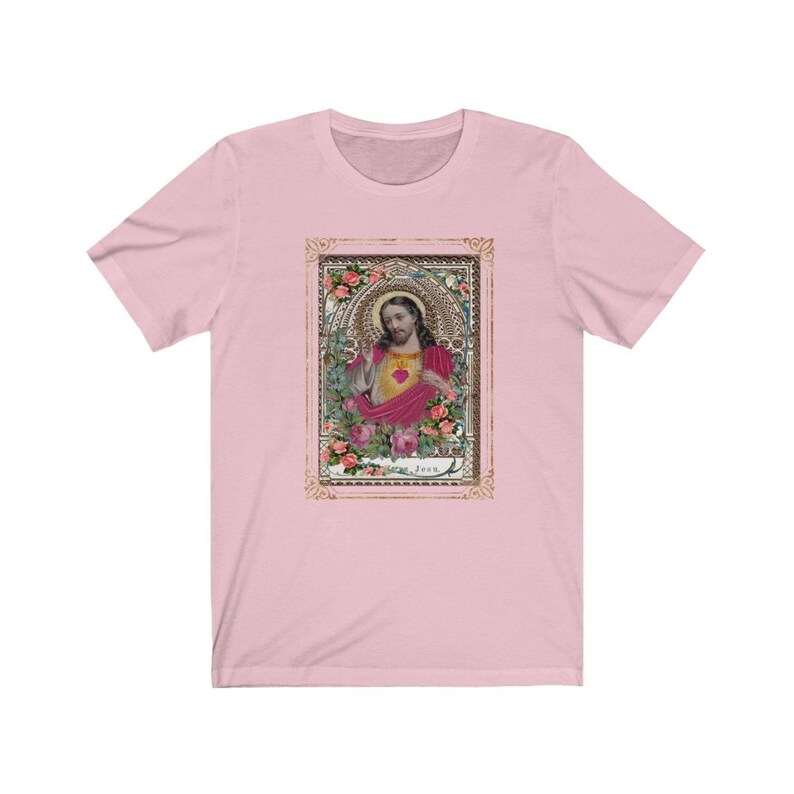 May include: A pink t-shirt with a vintage-style image of Jesus in a gold frame. The image features Jesus with a heart in his hand and roses surrounding him. The text "Jesus" is at the bottom of the image.