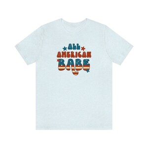 May include: Light blue t-shirt with a retro-style graphic that says "All American Babe" in red, white and blue with stars.