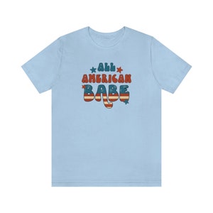 May include: Light blue t-shirt with a retro-style graphic that says "All American Babe" in red, white and blue with stars.