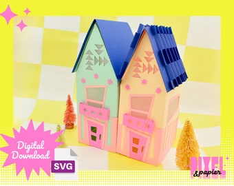 May include: Two papercraft houses with blue roofs and pink doors. The houses are decorated with geometric patterns and stars. The houses are sitting on a checkered background. The image includes the text "Digital Download" and "SVG".