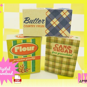 Puede incluir: Tres cajas de estilo vintage con etiquetas para "Mantequilla Fresca de Campo", "Harina de Calidad Premium" y "Azúcar de Caña Granulada Fina". Las cajas están apiladas una encima de la otra y tienen un patrón de cuadros.