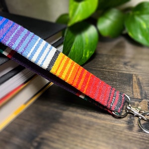 May include: A colourful woven wristlet key fob with a silver-tone clasp and key ring. The wristlet features a vibrant striped pattern in shades of red, orange, yellow, blue, and purple. The key fob is approximately 20 cm long.