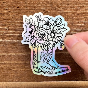 May include: A black and white line drawing of a pair of cowboy boots with a bouquet of flowers in the top of the boots. The boots are on a iridescent background.