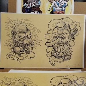 May include: Two black and white line drawings of Japanese mythical creatures. The first creature has three eyes and is holding a rope. The second creature has a large nose and is holding a fan.