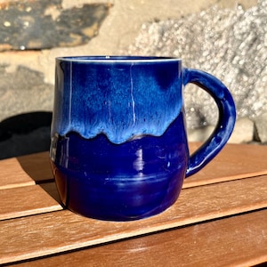 Puede incluir: Una taza de cerámica azul con un diseño de glaseado blanco. La taza tiene un cuerpo redondeado y un asa.