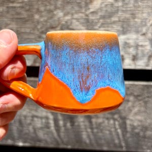 Taza de cerámica color naranja y azul con diseño de espresso.