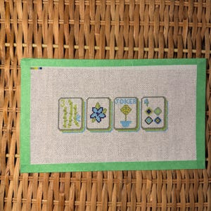 Op de afbeelding: Een borduurcanvas met een groene rand en het woord "TOKEN 4" weergegeven. Het canvas bevat vier vierkante ontwerpen met bloemen en geometrische patronen in groen- en blauwtinten.
