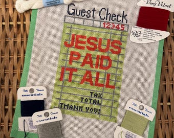May include: A needlepoint canvas featuring a grid design resembling a guest check with the text "Guest Check", "12345", "JESUS PAID IT ALL", "TAX", "TOTAL", and "THANK YOU!" in red and black, accompanied by five spools of embroidery thread.