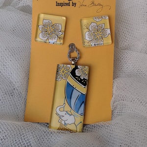 May include: A set of yellow and white floral patterned glass earrings and a matching pendant necklace with a blue and white hot air balloon and elephant design. The jewelry is inspired by Vera Bradley.