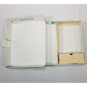 Op de afbeelding: Open witte vintage poppenkoffer met een handvat, een kleine lade en een kledingrek. De koffer is open en onthult de binnenkant. De koffer is gemaakt van wit materiaal met een witte sluiting.
