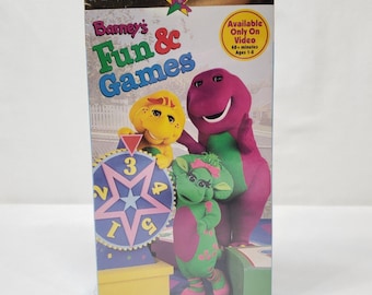 May include: A VHS tape for "Barney's Fun & Games" featuring Barney the dinosaur and friends. The cover has a colorful design with the title in large, playful letters. The tape is labeled "Available Only On Video" and is for ages 1-8.