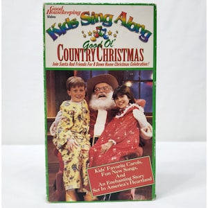 May include: A vintage VHS tape titled "Kids Sing Along Good Ol' Country Christmas." The cover features Santa Claus with two children, and the text "Join Santa And Friends For A Down Home Christmas Celebration!" is visible. The tape is green and white.