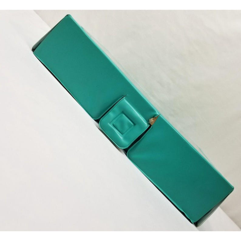 Op de afbeelding: Een turquoise rechthoekige doos met een vierkante inkeping aan de bovenkant. De doos is schuin, waardoor de randen en het bovenvlak zichtbaar zijn. De achtergrond is wit.