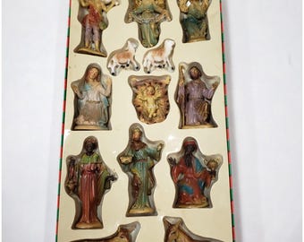May include: A nativity set featuring fourteen hand-painted figurines arranged in a plastic tray. The collection includes figures of a shepherd, angels, sheep, the holy family, three wise men, a cow, and a donkey, all with detailed colorful robes.