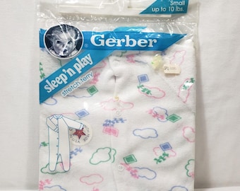 May include: A white Gerber sleep'n play stretch terry garment in plastic packaging. The fabric features a repeating pattern of pink, blue, and green clouds and geometric shapes. The label indicates a size small for up to 10 lbs.
