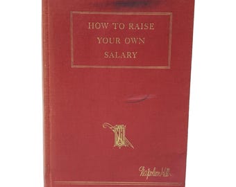 May include: A red hardcover book titled How to Raise Your Own Salary by Napoleon Hill. The front cover features gold lettering, a gold rectangular border, and a small gold emblem with the letters NHA. The book has a textured fabric finish.